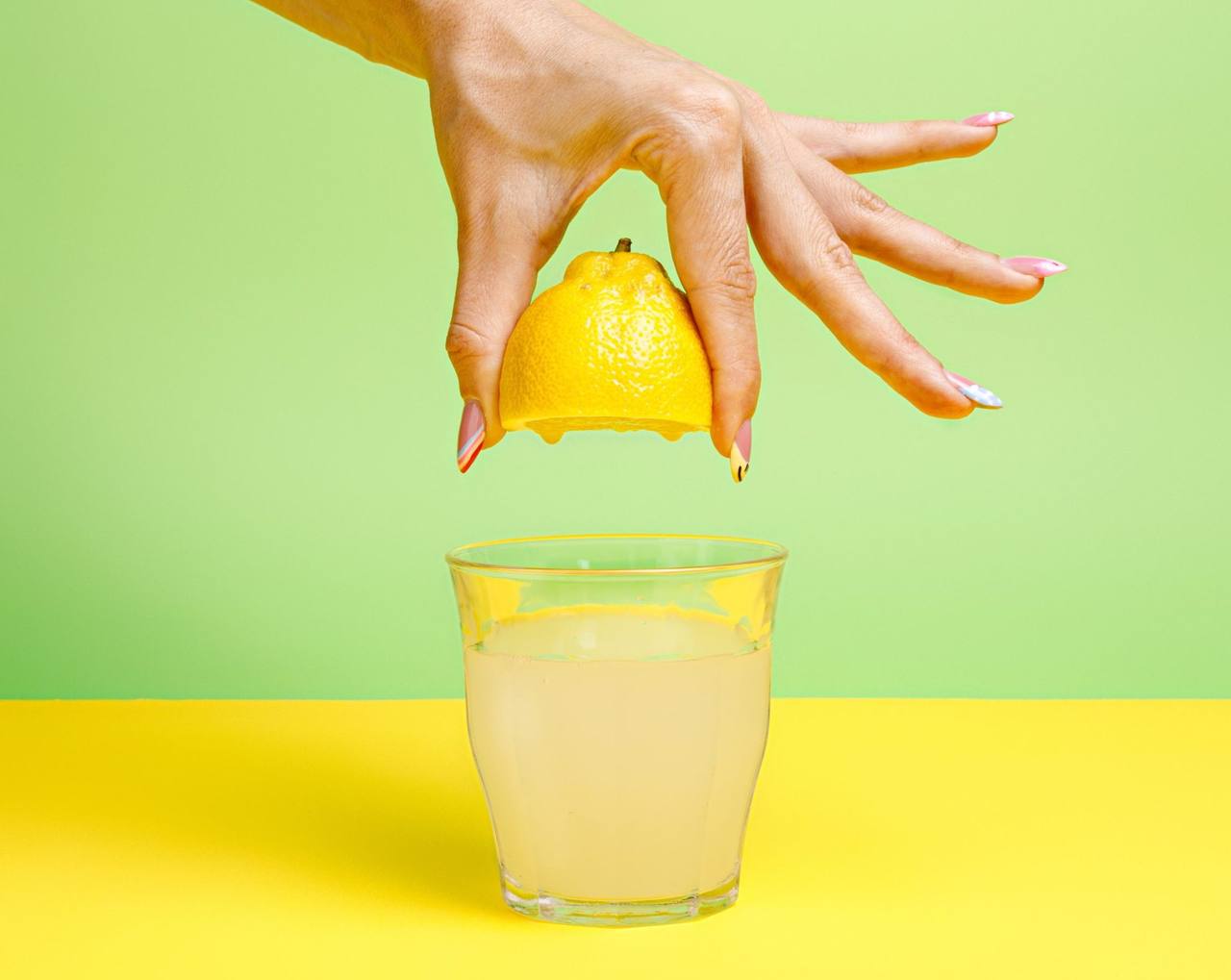 Met de hand een halve citroen uitknijpen boven een glas limonade